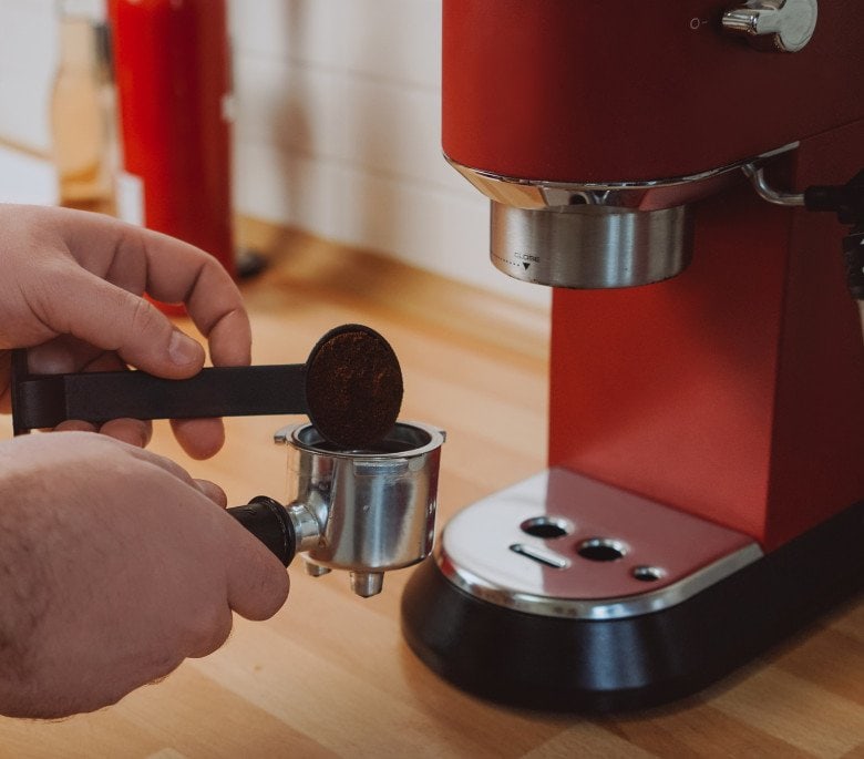 Red espresso machine and a person tamping with a plastic tool