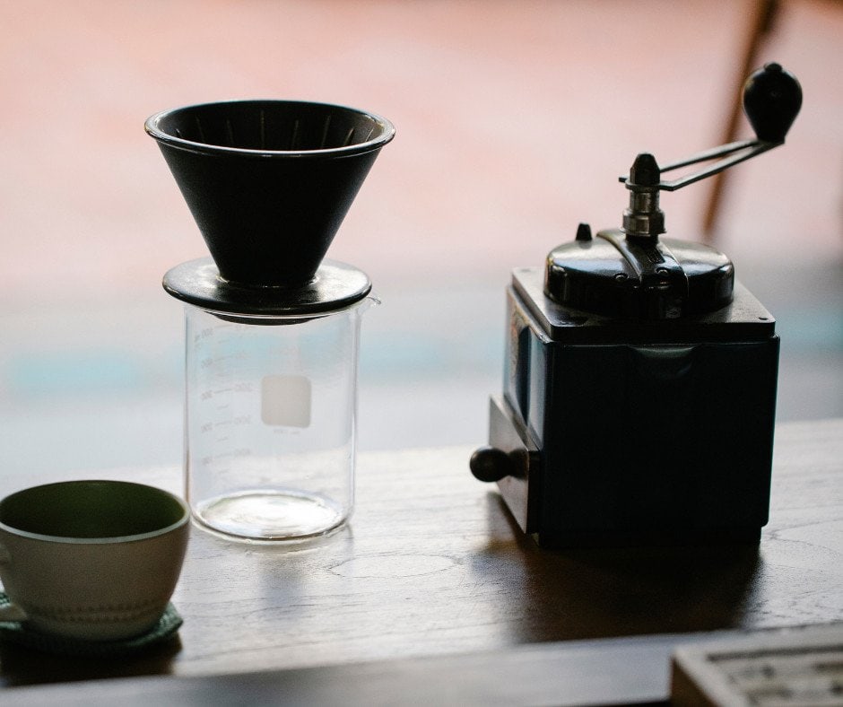 Cone dripper on top of a glass server. A wooden, vintage manual grinder is next to the dripper, and a modern cup is at the other side.

This is supplementary image for the article about the best grinder for pour-over coffee brewing.